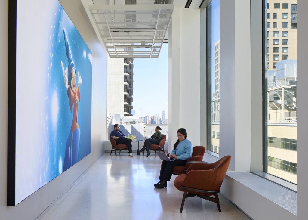 Employees sitting in a collaborative space with Disney artwork on the wall by Dave Burk &ndash; SOM &copy; 2024 Disney